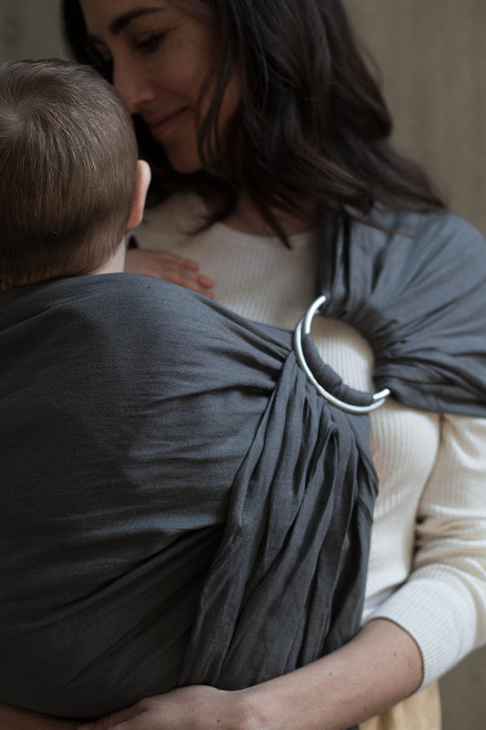 Mujer cargando a su bebé en rebozo de anillas o bandolera de lino color gris